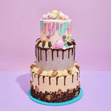 3 Tier Cake - Design Your Own with colorful pastel decorations, chocolate drips, and assorted toppings on each tier.